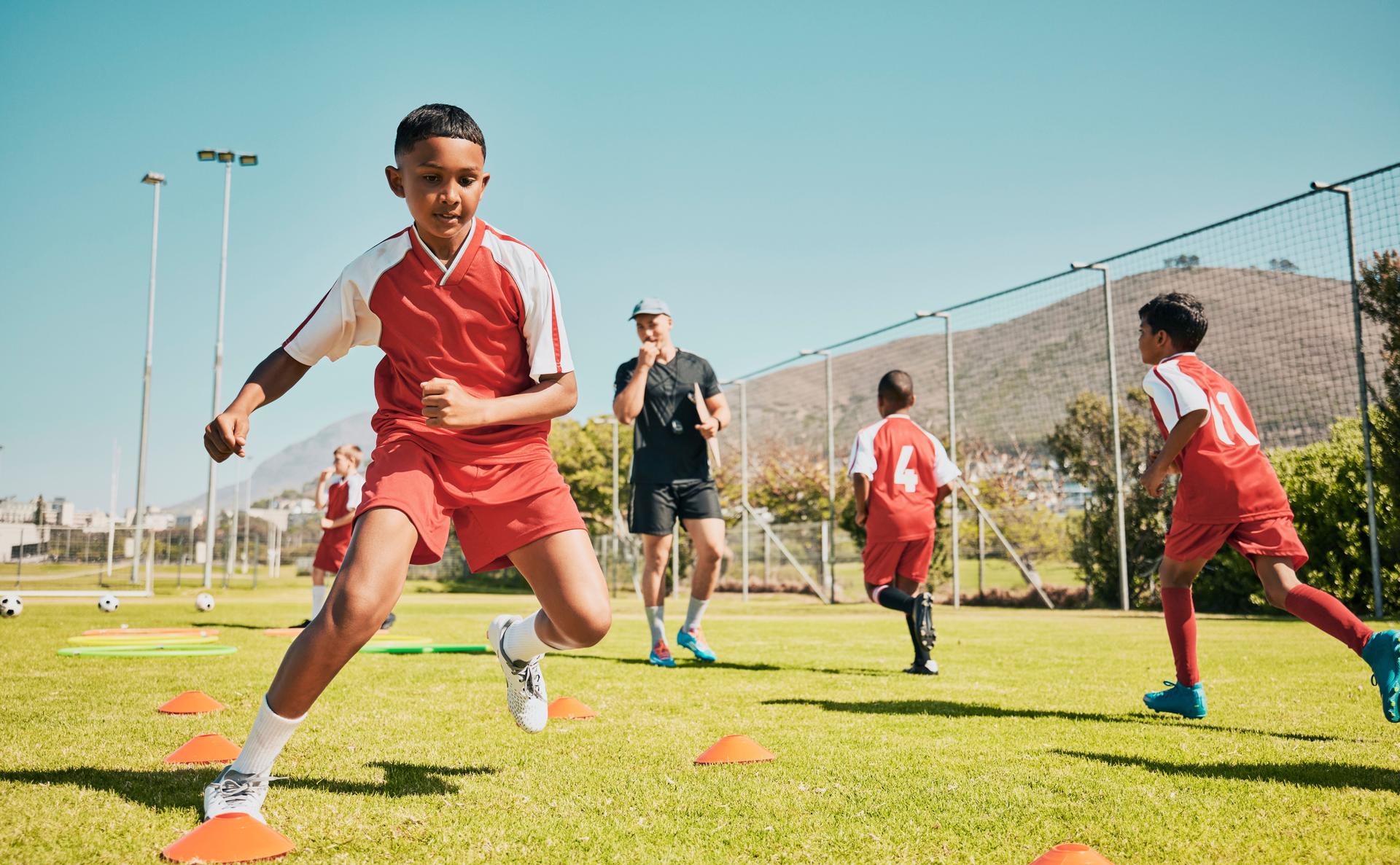 Fútbol, niños y entrenamiento o práctica para la competencia deportiva o juego en el campo de fútbol para el fitness, el ejercicio y la energía. Jugador de fútbol, cono y entrenador de deportes con niños al aire libre para la práctica del equipo