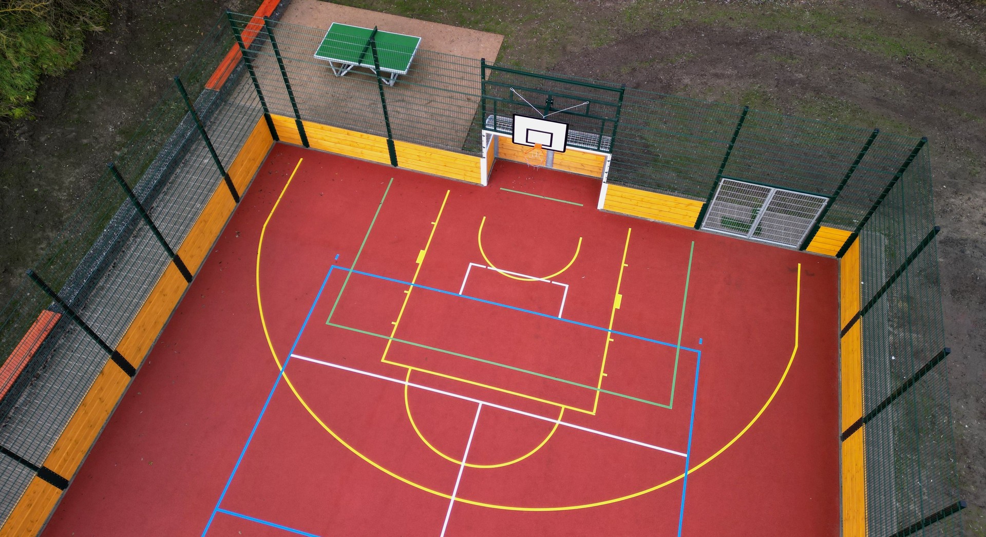 Parque infantil multifuncional al aire libre para juegos de pelota en la escuela. césped artificial verde de una alfombra de plástico con líneas. aros de baloncesto y porterías de fútbol. alrededor de la red alta de agarre y barandillas, tartán